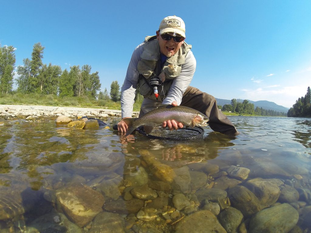 Angler crouching in shallow river water with a rainbow trout above a landing net