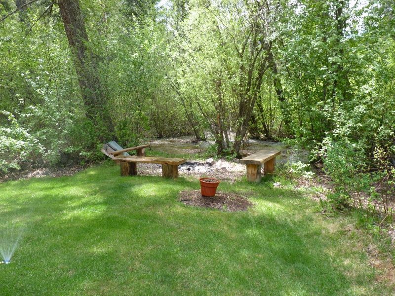 Tree-shaded cabin yard with outdoor seating beside a small stream