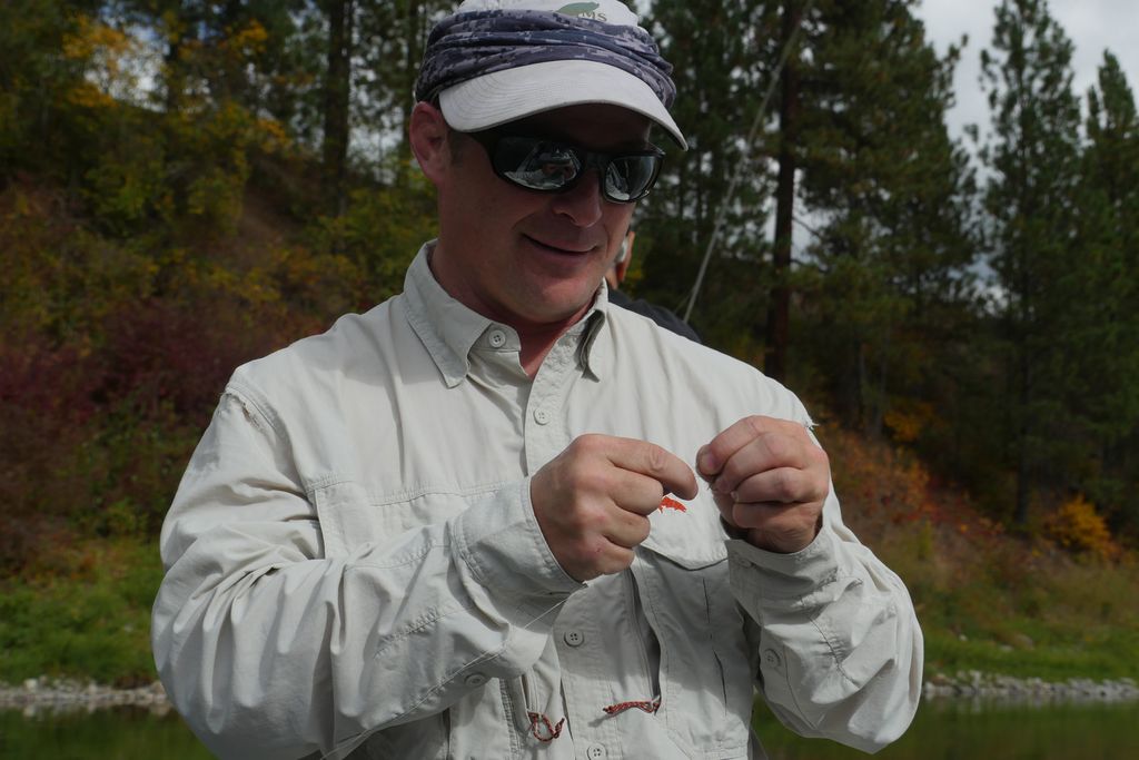 An angler in a fishing vest working on tackle beside the river