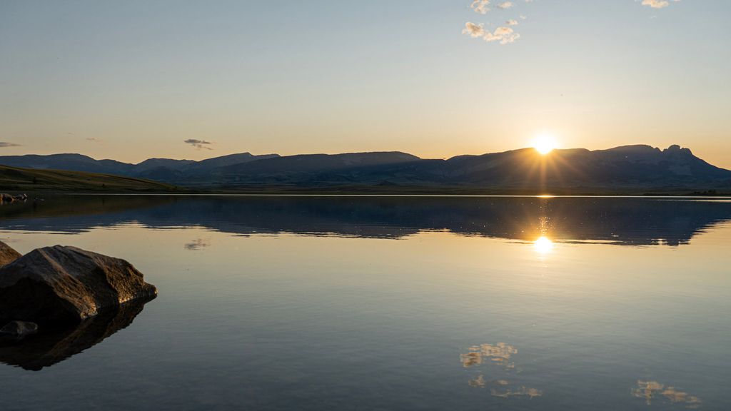 The setting sun reflected in still water below distant Central Montana hills