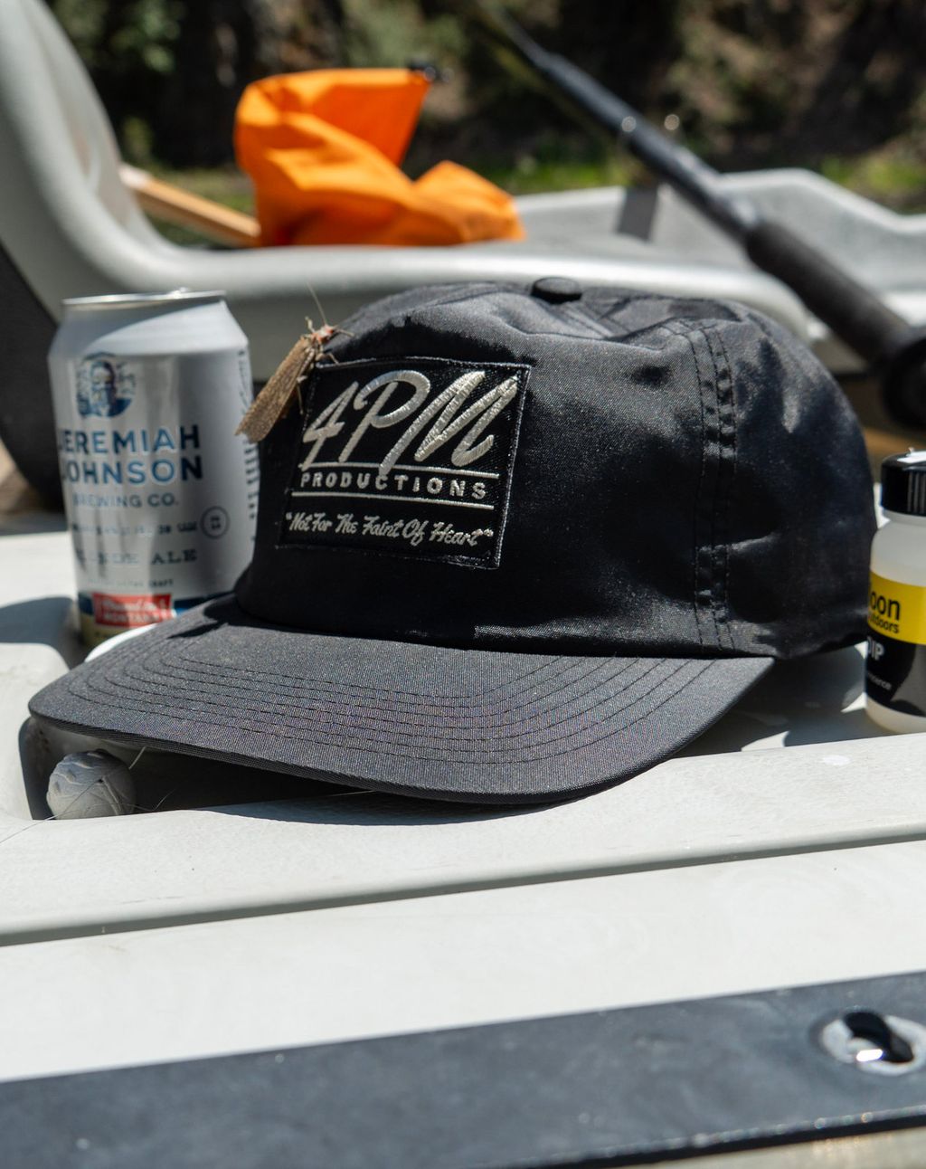 A 4PM Productions cap and a salmonfly beside fishing gear in a drift boat