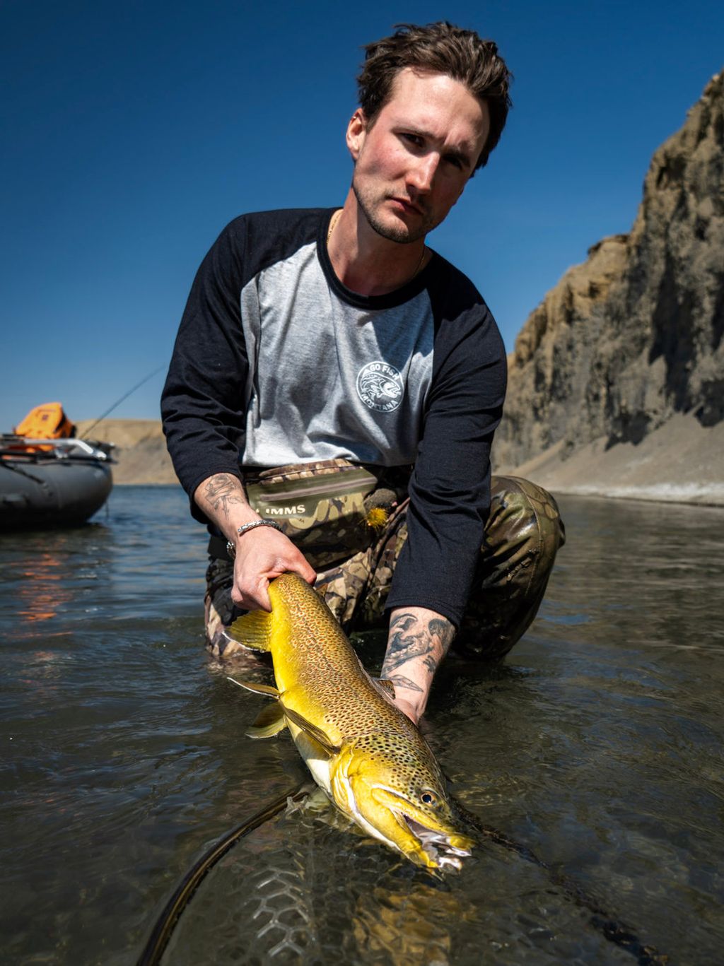 Angler wearing a gray GFM baseball tee with dark sleeves while holding a trout