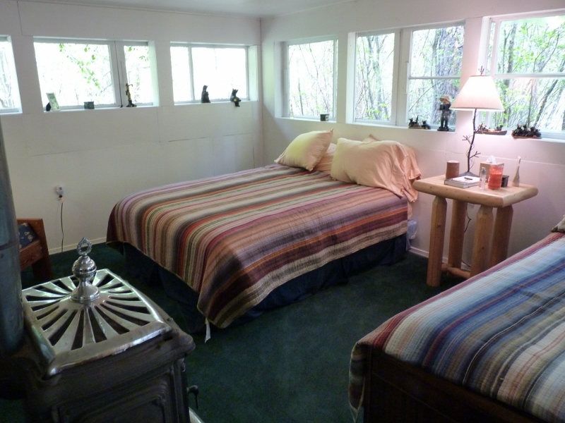 Two beds and a small table beside bright windows in a cabin bedroom