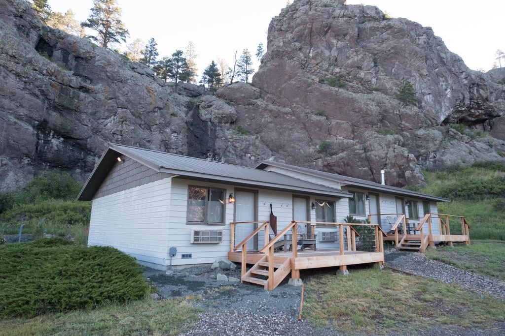 Light-colored cabin with a wooden deck beneath a rocky hillside