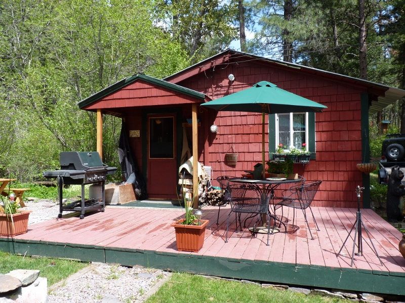 Red cabin with a deck, patio table and green umbrella among trees