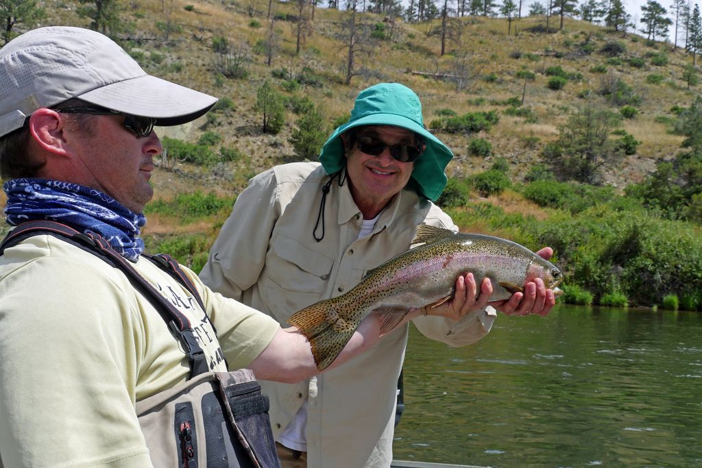 Guide and client holding a rainbow trout beside a drift boat on the Missouri River