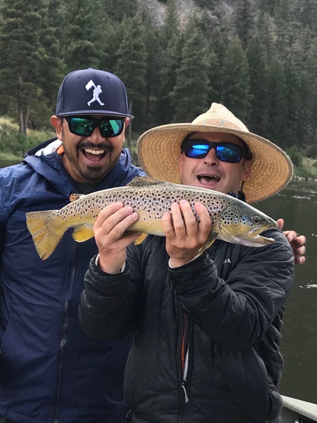 Two anglers in shallow river water with a brown trout
