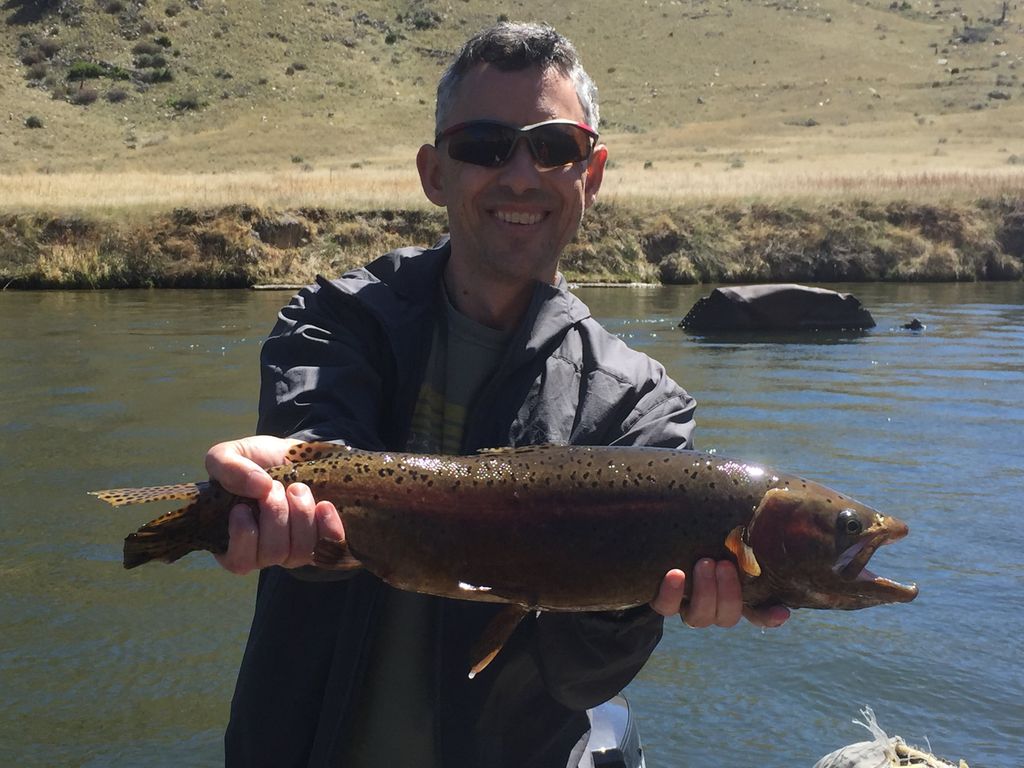 Angler holding a brown trout from a boat on calm river water