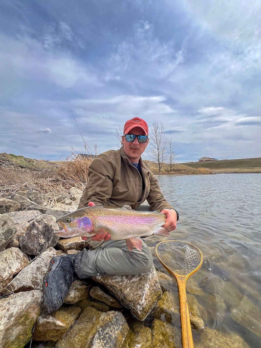 Seated angler holding a rainbow trout beside a Central Montana reservoir