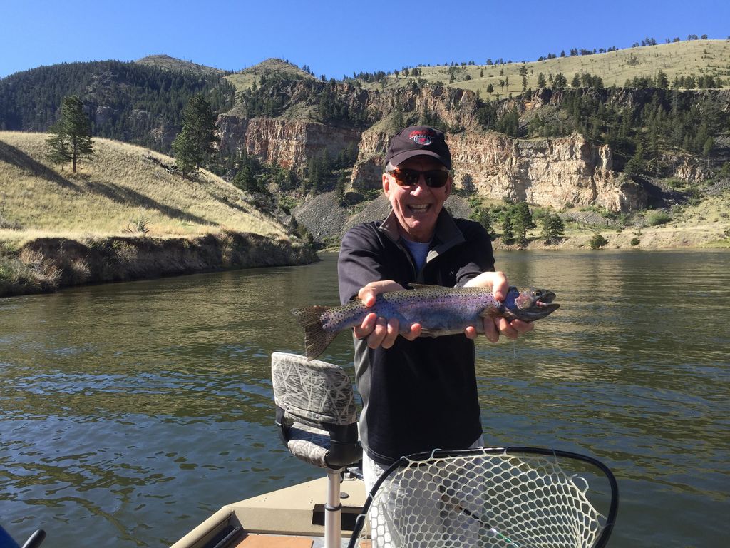Angler holding a rainbow trout in a boat beside rocky banks in the Gates of the Mountains area of Montana