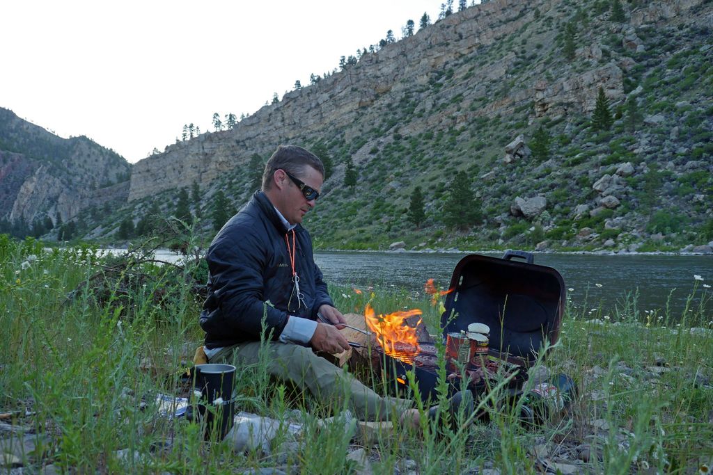 Guide preparing lunch on a small grill beside a river